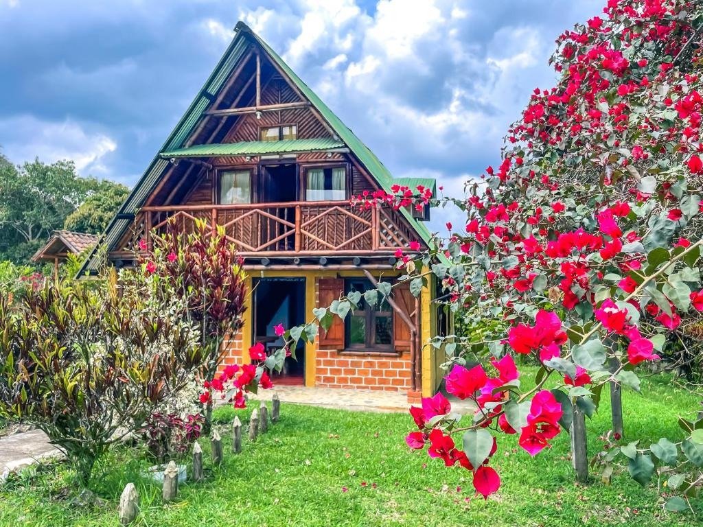 Cabaña de diseño alpino triangular en madera rodeada de naturaleza y flores rojas