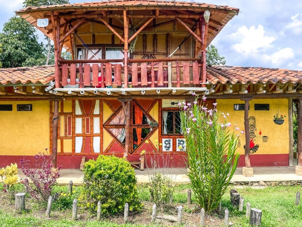 Fachada exterior de Cabañas Numbana con dos pisos en madera y paredes amarillas rodeada de flores